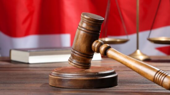 Judge's gavel, book and scales on wooden table against flag of United Kingdom-Shutterstock_2680090199